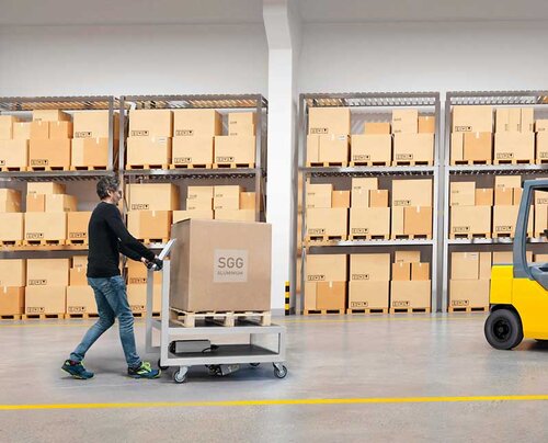 Ein Mann schiebt einen Transportwagen, der mit einem großen Karton beladen ist, durch eine Logistikhalle